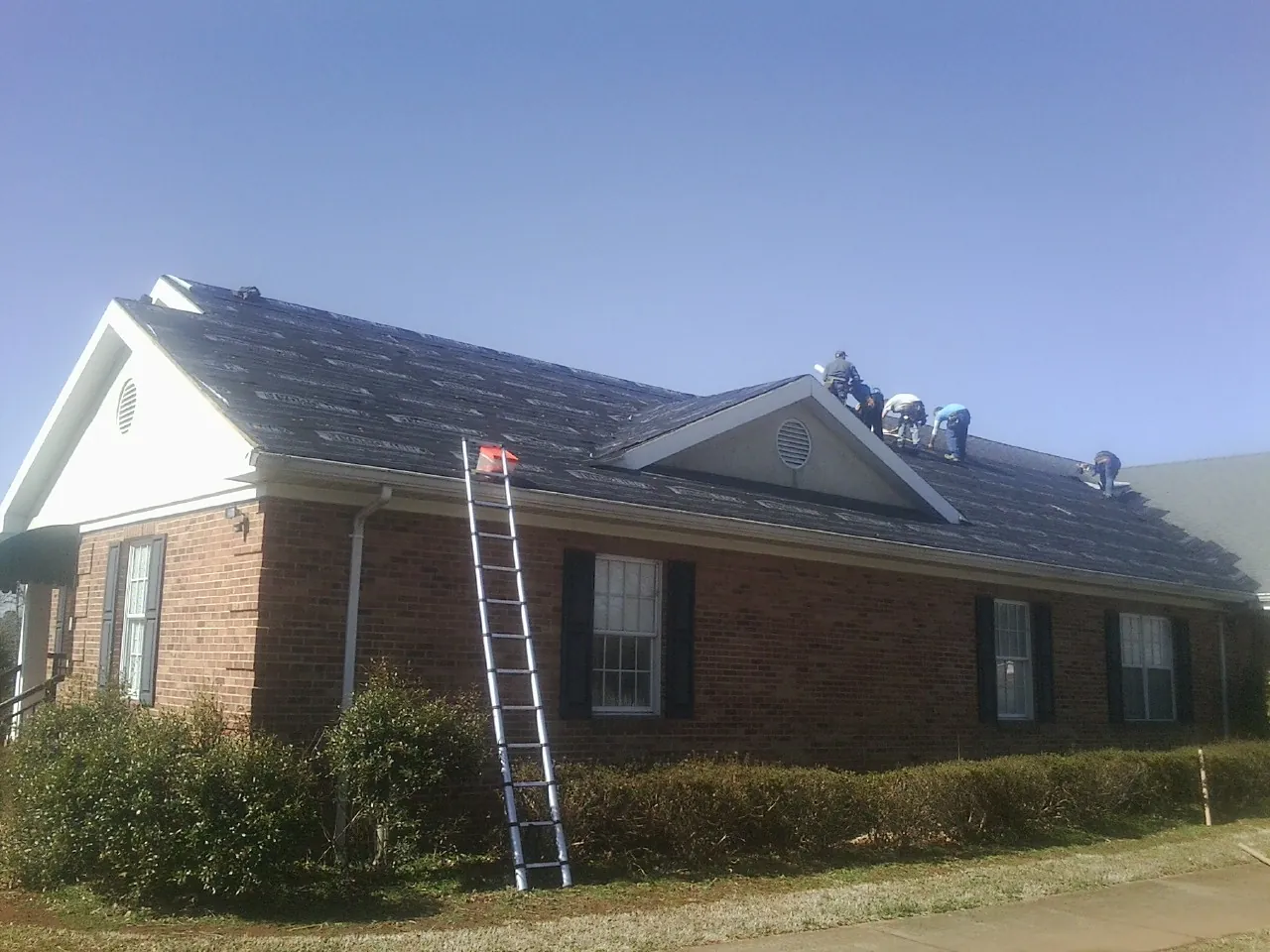Crew tearing shingles off a brick ranch roof with a ladder set — Emergency Roof Repair work by our crew in Bourbon