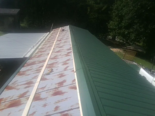 Old rusted panels beside newly installed green metal roofing — Wind Damage Roof Repair by Roofing Brothers in Bourbon