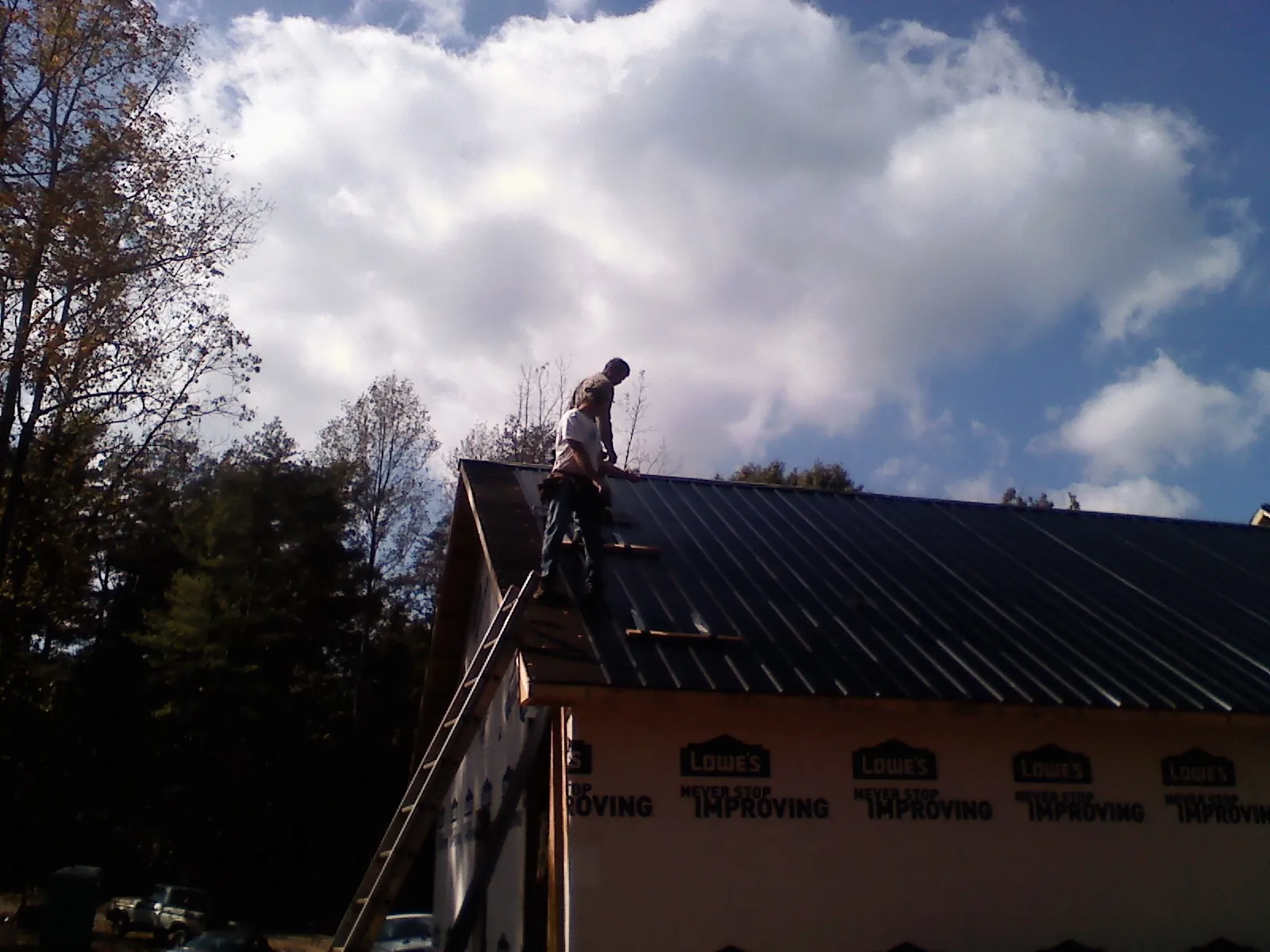Roofer fastening dark metal panels high against a cloudy sky, from a Roof Inspection job in Bourbon