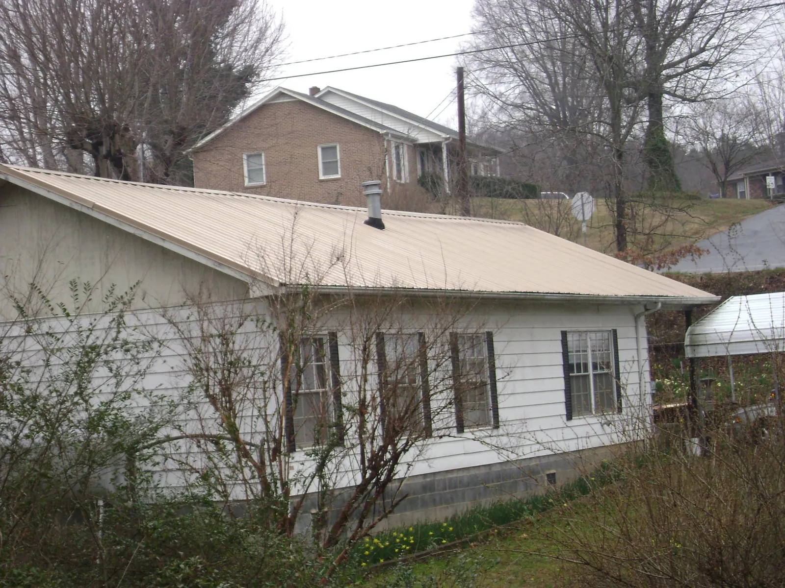 Tan metal roof on a white sided house set into a hillside — Commercial Roofing by Roofing Brothers in Bourbon
