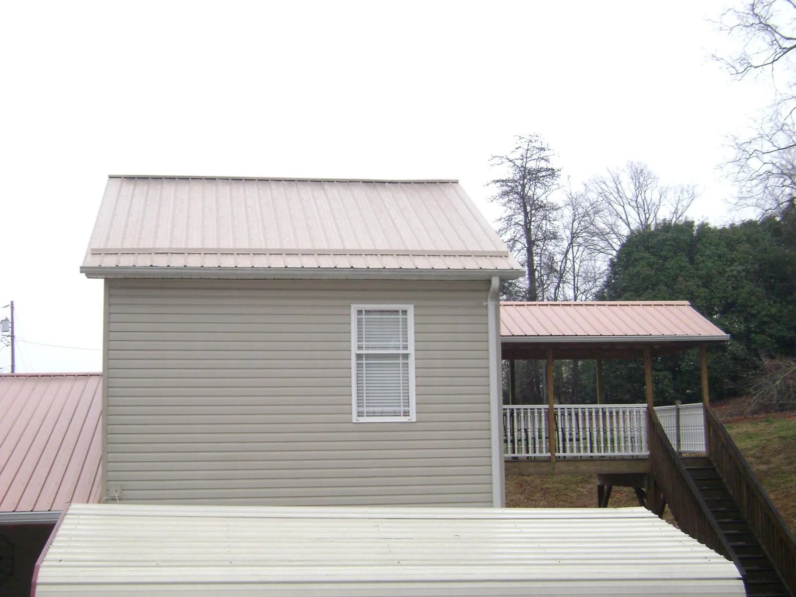 Tan metal roofs on a two story addition and attached porch, from a Roof Replacement job in Bourbon